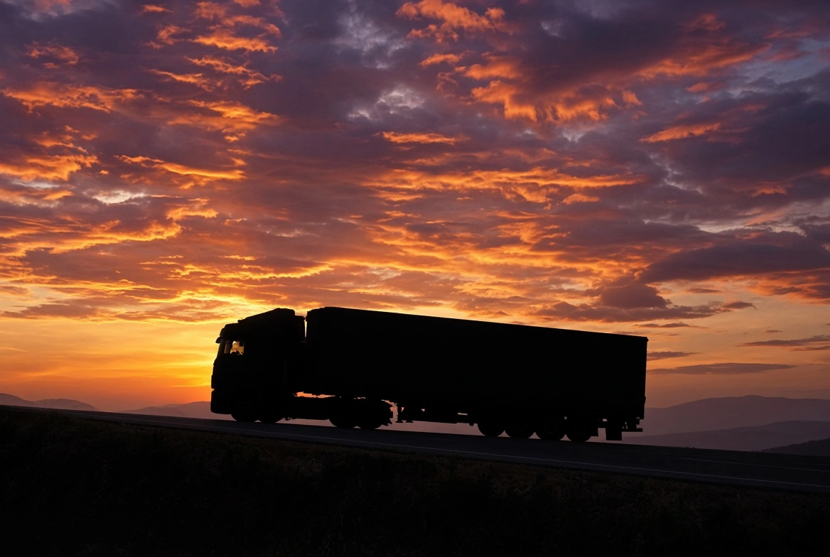 Silhueta de caminhão em rodovia ao entardecer.